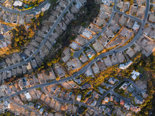 Aerial view of a suburban dreamscape where golden light bathes houses nestled along winding roads, casting deep shadows, Los Angeles, California, United States.