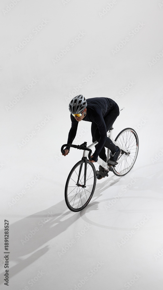 Fototapeta premium Road cyclist in aerodynamic position riding bicycle in studio. Concept of professional cycling, speed optimization, racing posture, performance training, competitive sport, minimal background.