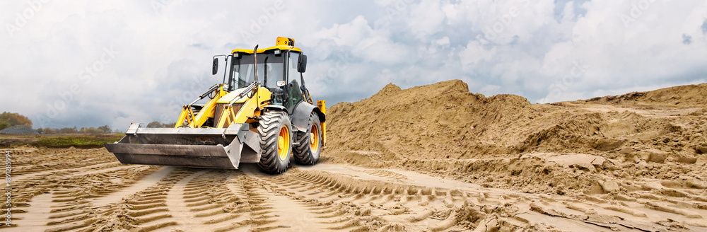 Obraz premium A loader uses its bucket to grade a construction site. Space for text