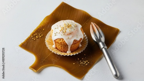 Gourmet lemon or vanilla cupcake with white glaze and sprinkles served on a brown leather or fruit leather square next to a metal citrus reamer on a light textured surface