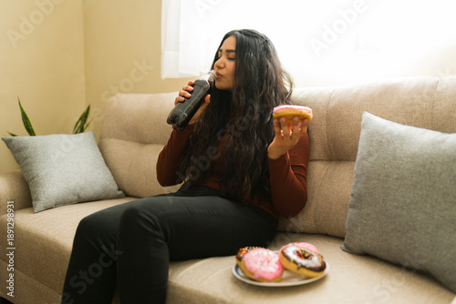 Tableau sur toile Woman relaxing on sofa, enjoying sugary snack and soda drink, embracing indulgen