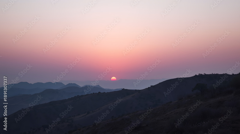 Fototapeta premium Sunset over the Mountains: The sun dips below the horizon, painting the sky with fiery hues, silhouetting the rugged mountain range in a display of natural grandeur.
