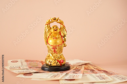 Wallpaper Mural A statue of a smiling Buddha with money on a pink background. Torontodigital.ca