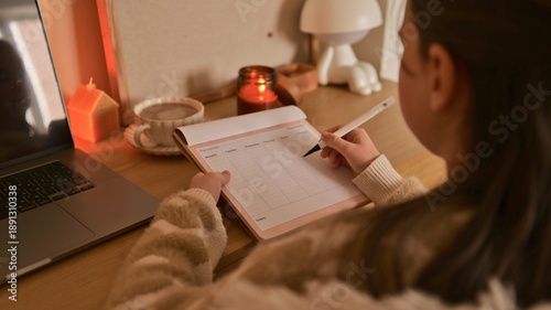 Young person writing in a weekly planner next to a laptop and coffee