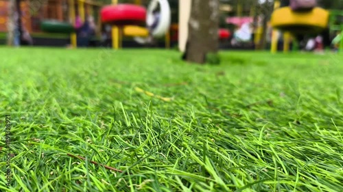 Green grass with blurred background of colorful swings in a playground that move slowly
