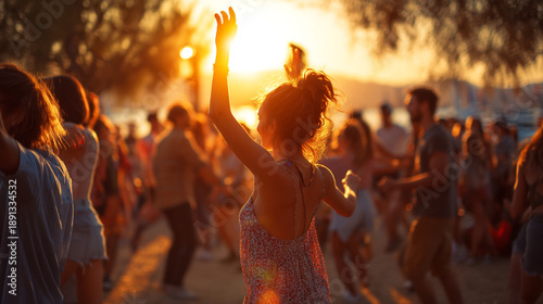 A woman dances with her arm raised in a crowd during a vibrant outdoor festival at sunset