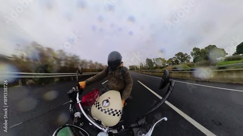 Toma en 4k de hombre conduciendo moto tipo scrambler mientras llueve por carretera