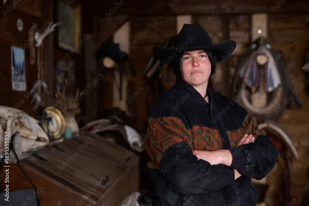 Fototapeta premium Cowgirl in a hat stands with arms crossed inside a rustic ranch workshop