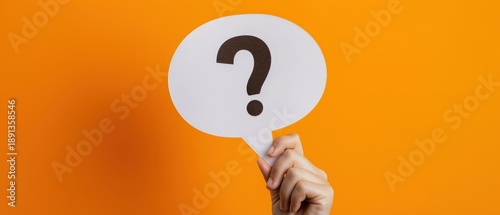 Fototapeta Hand holding white speech bubble with question mark on bright orange background, representing question, inquiry, help, communication, support, problem solving and information concept.
