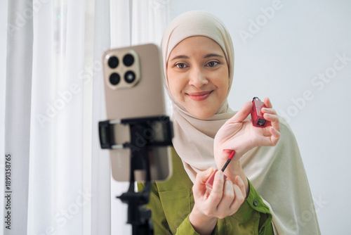 A cheerful Asian woman applies lipstick while vlogging on a smartphone mounted on a tripod. Soft natural light creates a warm, approachable vibe suitable for beauty, fashion, and lifestyle content.