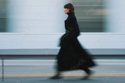 Woman in black coat walking on street with motion blur effect, urban fashion