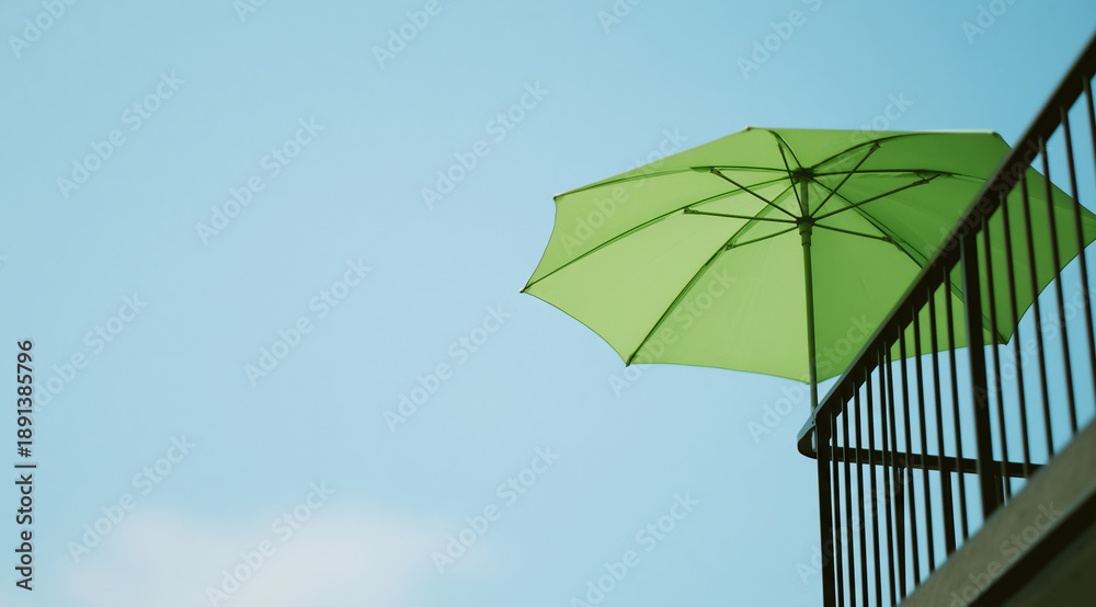 Fototapeta premium Bright green patio umbrella against a clear blue sky, offering shade on a sunny day