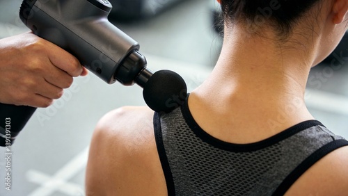 Massage gun therapy on female athlete shoulder for muscle recovery