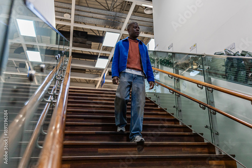 Fotografie A young Black man walks down wooden stairs in a shopping mall