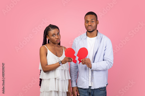 Canvastavla Disappointed black man and woman holding two pieces of broken paper heart standing isolated over pink studio background