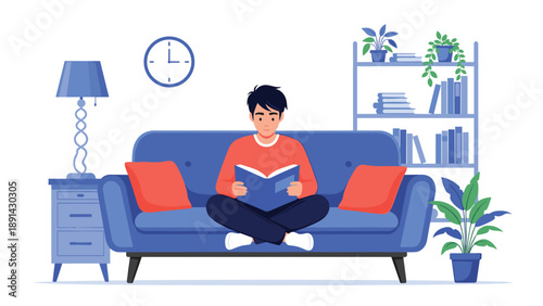 Young man sitting comfortably on a blue sofa and reading a book in a modern living room with a bookshelf and lamp.