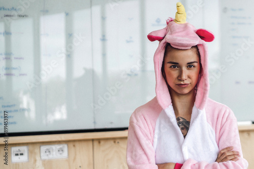 Woman wearing unicorn onesie, standing in front of whiteboard, looking stubborn