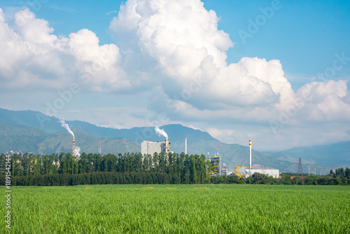 A panoramic view of an industrial site in Valle del Cauca, Colombia, with vibrant green fields and a backdrop of mountains under a bright blue sky.