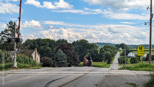 Foto A horse and buggy move slowly across a rural road near train tracks