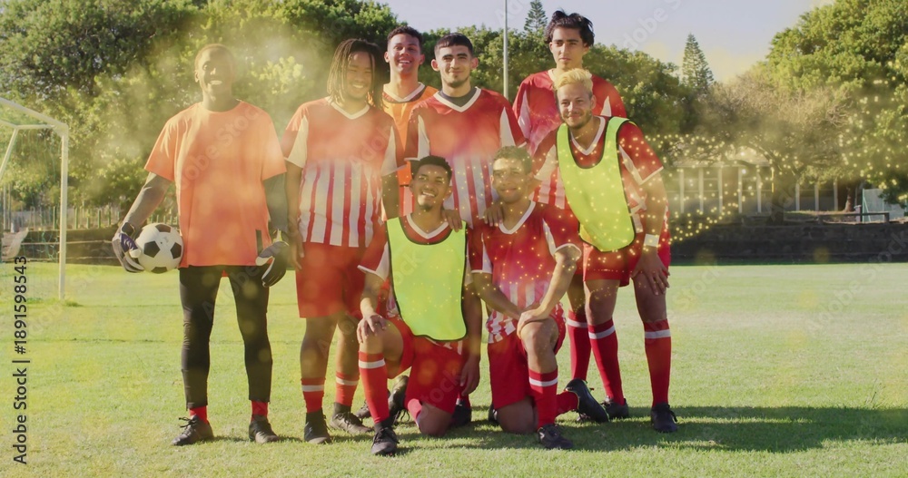 Fototapeta premium Posing eight soccer players wearing red kits with yellow vests on grassy field, keeper holding ball