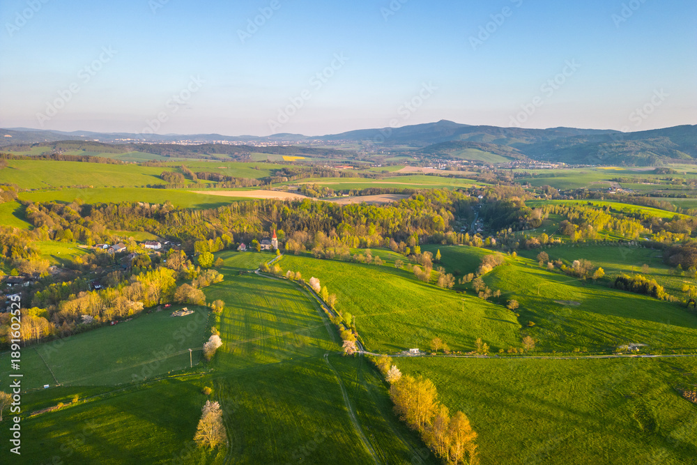 Obraz premium A summer landscape with fields and trees. The land is green with hills in the background. The scene captures nature in its seasonal form.