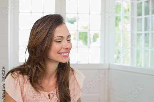 Mid-adult woman sitting in sunroom near grid windows with white wall and sill smiling looking right Free Download Mid-adult woman sitting in sunroom near grid windows with white wall and sill smiling looking right - GFXLoad