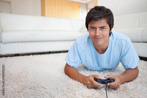 Billede på lærred Adult male lying on light shag rug in living room wearing blue tee, holding wire