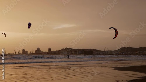 Kiteboarders catching air at sunset on the coast.