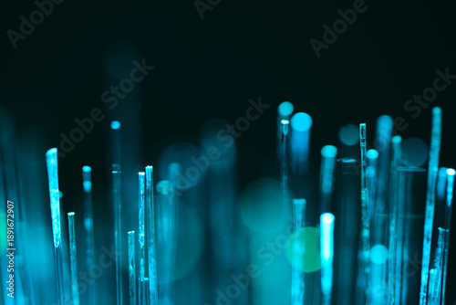 Macro shot glowing fiber optic cable ends emitting soft teal and cyan light against dark background. Concept of high speed internet and data transmission.