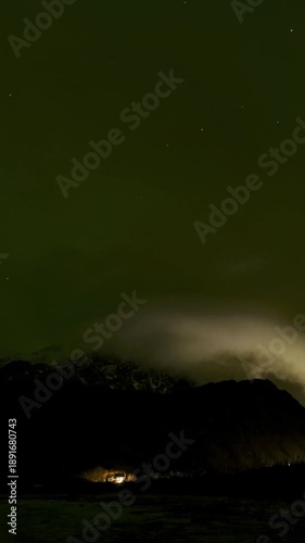 Starry Sky, Northern Lights and clouds above mountains surrounding sandy shore. 4K Vertical 9:16   Time Lapse. Lofoten Islands, Northern Norway