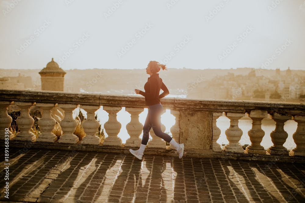 Fototapeta premium Woman jogging during sunset near a stone railing in Malta