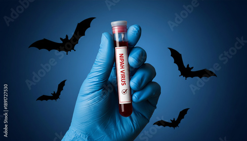 gloved hand wearing bright blue nitrile medical gloves holding a transparent laboratory test tube filled with red blood. The tube has a white label reading “NIPAH VIRUS” in bold red capital letters.