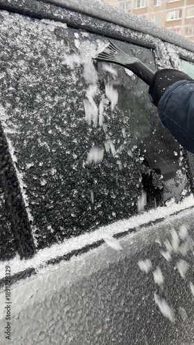 Person clearing heavy ice from car window with plastic scraper. Cold winter morning and routine vehicle preparation. Vertical video.