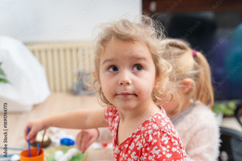 Fototapeta premium Young child paints at a table with bright colors in a room with friendly atmosphere during daytime
