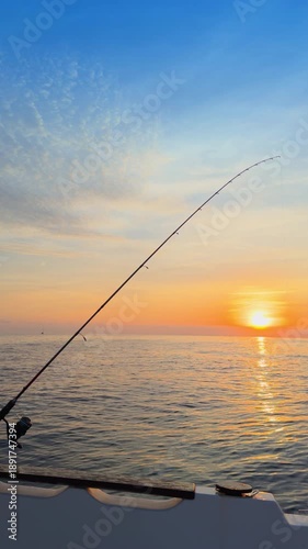 Offshore bottom fishing at sunset from boat with rod over calm sea