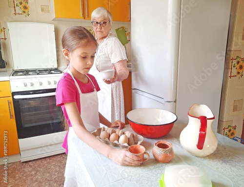 A grandmother and her granddaughter set out the necessary ingredients for cooking on the table.