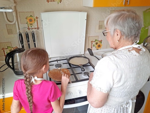 A granddaughter helps her grandmother make pancakes in the kitchen.