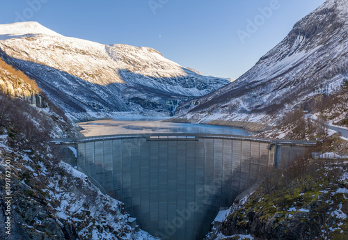 Hoover dam, power plant with snow-covered mountains cradle a massive concrete dam above a frozen lake. Location Tafjord in Norway.