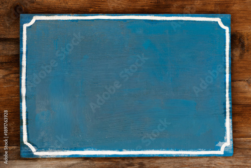 Blank wooden sign with peeling blue paint and a white border, nailed to a natural wood wall.