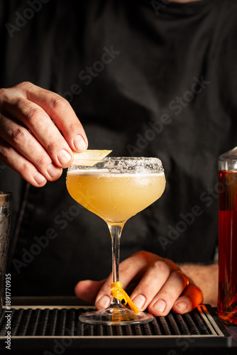 Preparing a margarita cocktail in a bar. Cold drink consisting of tequila, triple sec, and lime juice, served with salt on the rim of the glass.  Black background, vertical image.