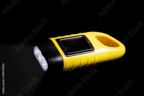 Yellow Solar and Hand Crank LED Emergency Flashlight with Carabiner Isolated on Black Background, Rechargeable Torch for Camping and Power Outages