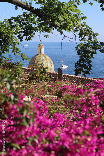 CHURCH OF SANTA MARIA ASSUNTA IN POSITANO with a beautiful multicolored majolica dome and blooming bright red-pink bougainvillea flowers
