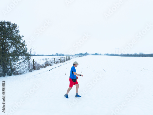 A man jogging across a snowy field in a T shirt and a shorts thus improving his health.
