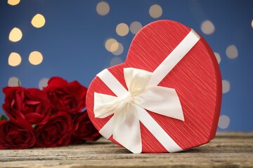 Saint Valentine's day. Beautiful heart shaped gift box and roses on wooden table against blue background with blurred lights, closeup
