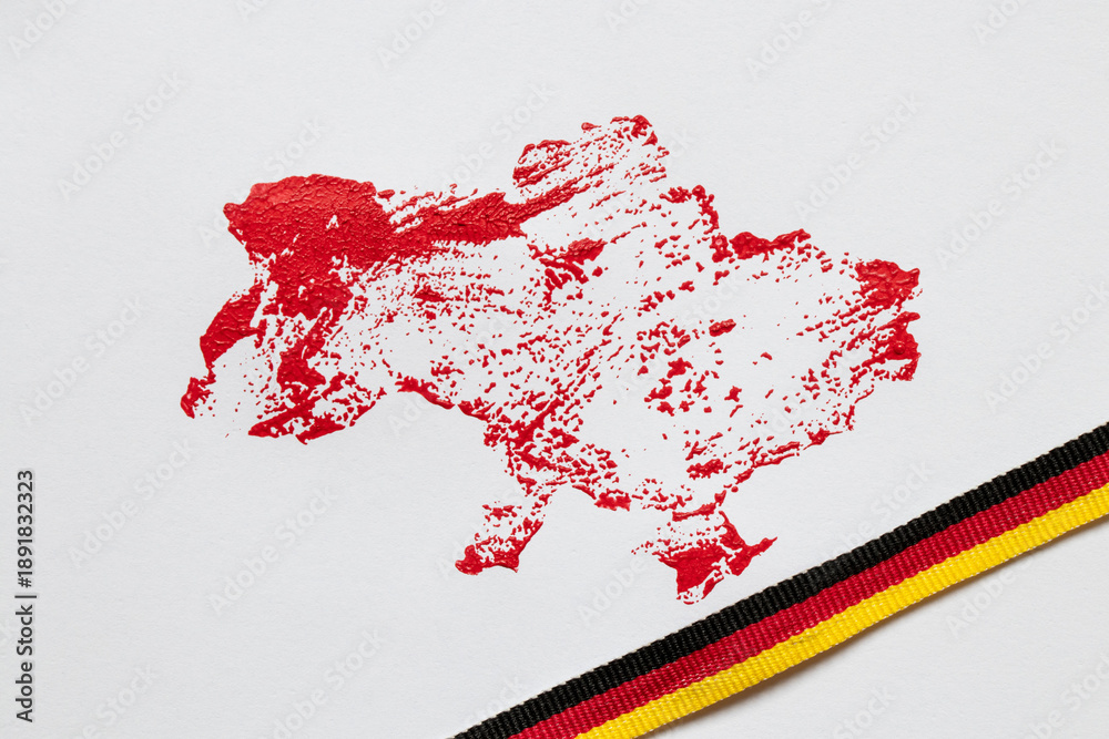 Fototapeta premium The outline of the map of Ukraine, drawn in red paint and the ribbon of the German flag on a white background, imitation of blood, support