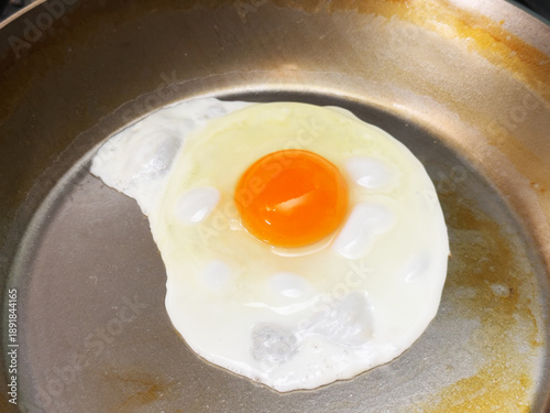 Closeup of a hen’s egg with yolk and white being cooked sunnyside up, in a very lightly oiled, frying pan.