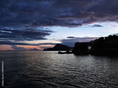 Tranquil harbor city nestled beneath mountains as evening falls and lights sparkle on water