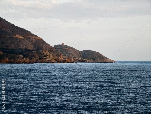 Historic tower atop rocky seaside cliffs, Calm waters beside ancient rugged coastal landscape with tower