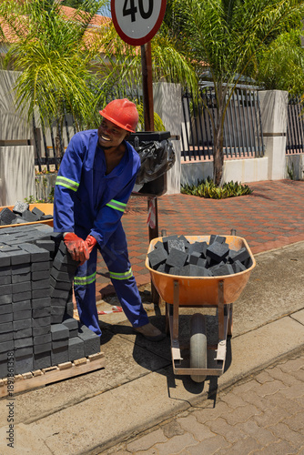 african construction worker laying dark grey brick pavers on residential sidewalk.