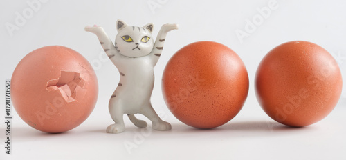 Tableau sur toile Plastic kitten figure reacting to a cracked egg among whole ones on white background
